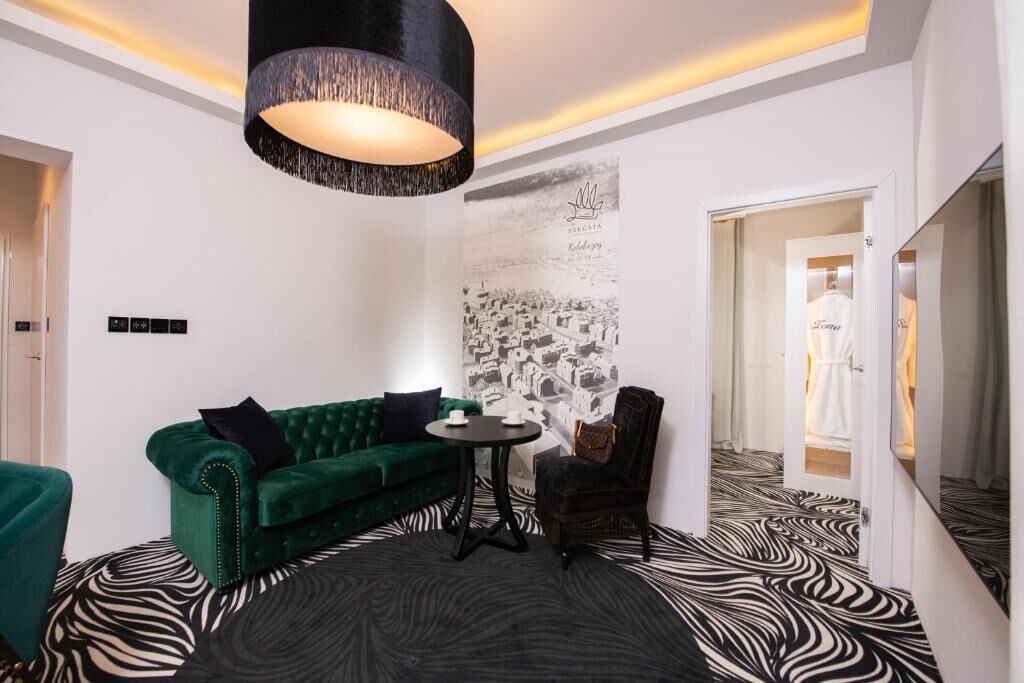 A room with a green sofa, a round table, a chair, a zebra-patterned floor, a large wall mural, and a hanging light fixture.