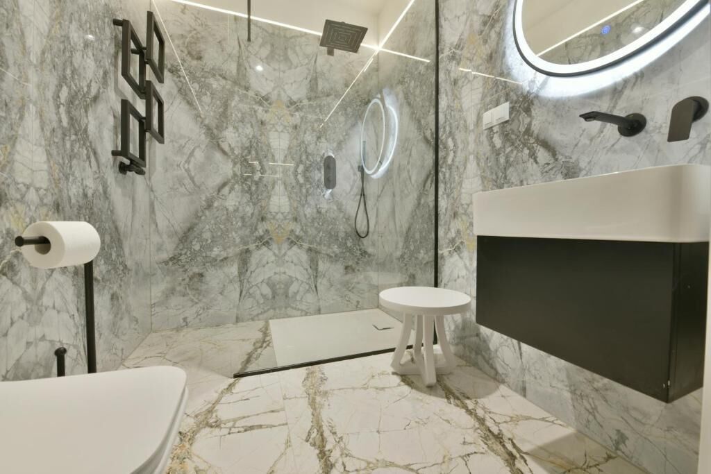A modern bathroom with a marble floor, a round mirror, a toilet, and a shower.