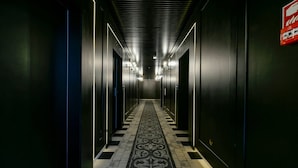 A long, narrow hallway with a patterned carpet, metal elevator doors, and a red exit sign on the right wall. - Fregata Kołobrzeg (Kolobrzeg)