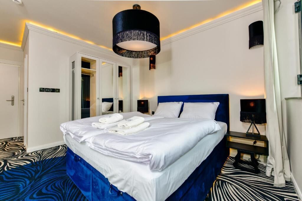 Una habitación de hotel con una cama grande, un armario, un espejo, una mesita de noche y una lámpara en el techo.