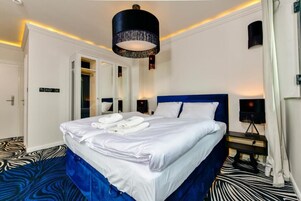 Una habitación de hotel con una cama grande, un armario, un espejo, una mesita de noche y una lámpara en el techo.