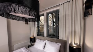 A modern bedroom with a large bed, two bedside tables, a black lamp, and a view of trees through the window. - Fregata Kołobrzeg (Kolobrzeg)