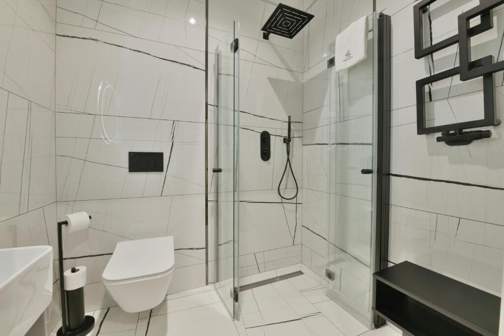 Une salle de bain moderne avec une douche à parois de verre, des toilettes blanches et une étagère noire.