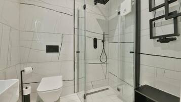 Une salle de bain moderne avec une douche à parois de verre, des toilettes blanches et une étagère noire.