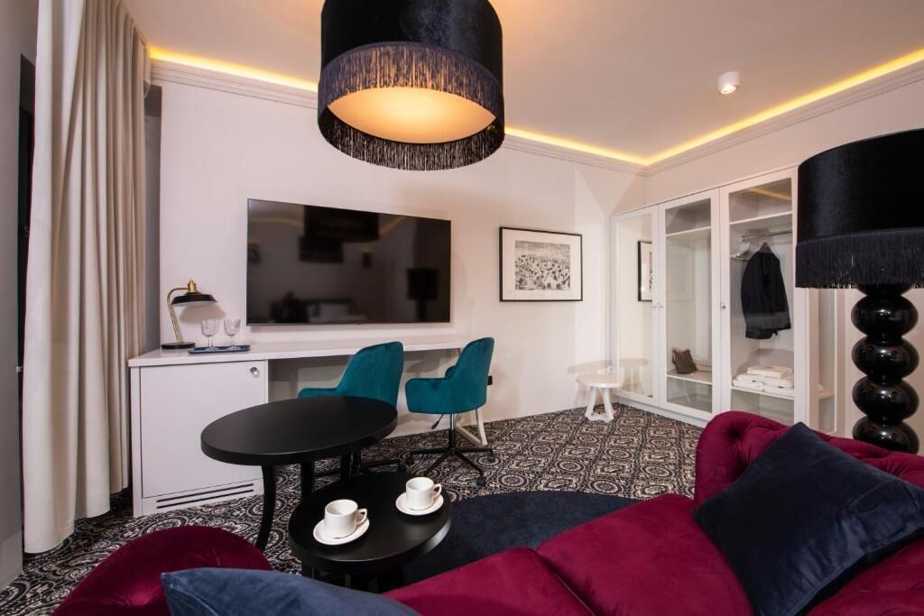 A modern living room with a black sofa, teal chairs, a black table with cups, a TV, and a wardrobe.