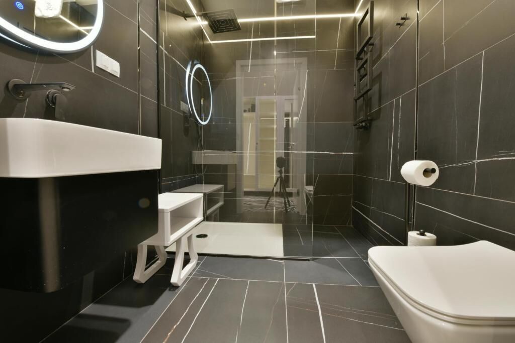 A modern bathroom with a large mirror, a toilet, and a sink.