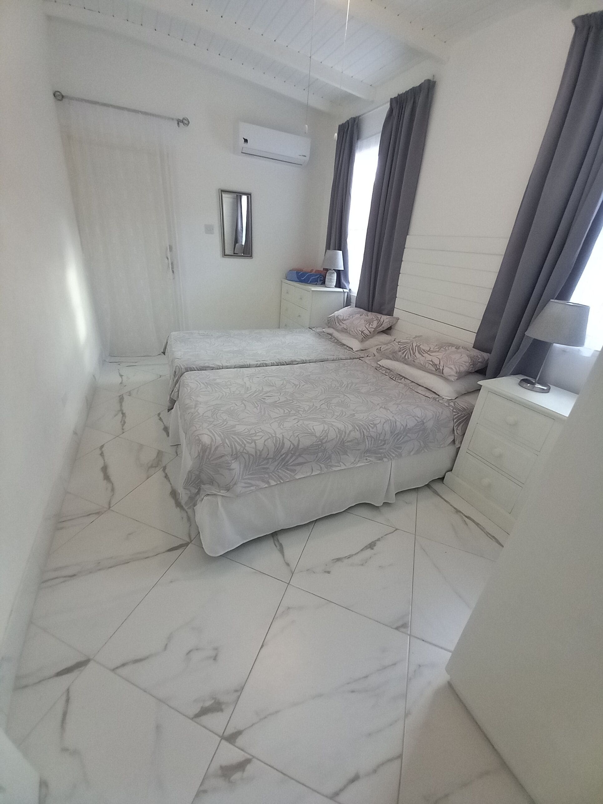 Ein Schlafzimmer mit zwei Betten, einem Nachttisch, einer Kommode, einer Klimaanlage und einem Fenster mit Vorhängen.