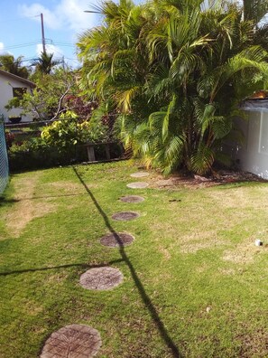 A well-maintained garden with a stone pathway, lush greenery, and a palm tree. - Garden Apartment modern clean and well kept, comfortable cool burglar bars nets (Mount Standfast)