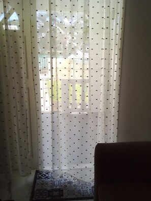 A room with a patterned curtain, a patterned rug, and a view of the outside. - Garden Apartment modern clean and well kept, comfortable cool burglar bars nets (Mount Standfast)