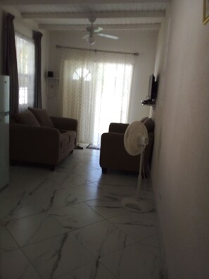 A living room with a ceiling fan, two sofas, a TV mounted on the wall, and a tiled floor. - Garden Apartment modern clean and well kept, comfortable cool burglar bars nets (Mount Standfast)