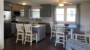 A modern kitchen with a central island, white chairs, and a dining table with a bowl.
