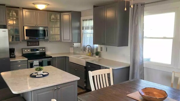 A modern kitchen with grey cabinets, a microwave, an oven, and a sink. There is a dining table with chairs and a wooden bowl on a placemat.