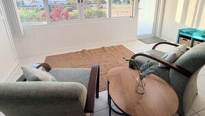 Une pièce avec une grande fenêtre, un tapis marron, une table en bois et un canapé vert.