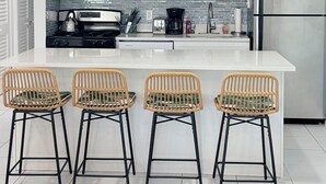 Une cuisine moderne avec des meubles blancs, des appareils en acier inoxydable, un îlot central doté de tabourets et un éclairage suspendu.