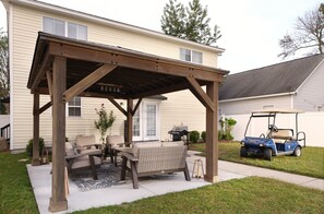 Eine überdachte Terrasse mit Gartenmöbeln, einem Golfwagen und einem Haus im Hintergrund.