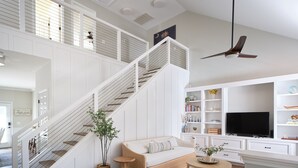 Un salon spacieux avec un escalier en bois, un canapé confortable, une télévision et une bibliothèque.