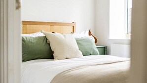 Een bed met een houten hoofdbord en twee kussens, één groen en één wit.