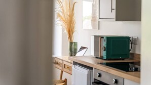 Een moderne keuken met een groene magnetron, houten kastjes en een vaas met gedroogde planten.