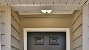 A dark brown front door with a rectangular design, flanked by white siding and a small porch area with a light-colored roof. - Golden Springs Stepless Rancher with GAMEROOM! (Anniston)