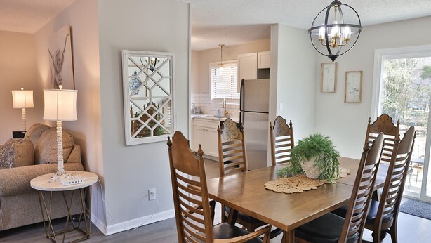 A dining area with a wooden table, six chairs, a chandelier, and a potted plant. - Golden Springs Stepless Rancher with GAMEROOM! (Anniston)