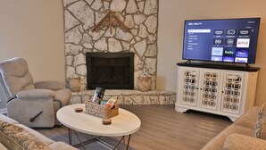A cozy living room with a stone fireplace, a flat-screen TV, and comfortable seating. - Golden Springs Stepless Rancher with GAMEROOM! (Anniston)