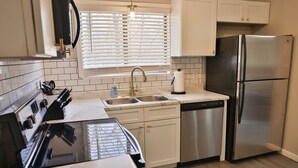 A modern kitchen with white cabinets, a stainless steel refrigerator, a dishwasher, and a stove. - Golden Springs Stepless Rancher with GAMEROOM! (Anniston)