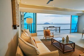 Ein Wohnzimmer mit einer Couch, einem Couchtisch und Blick auf das Meer durch große Fenster.