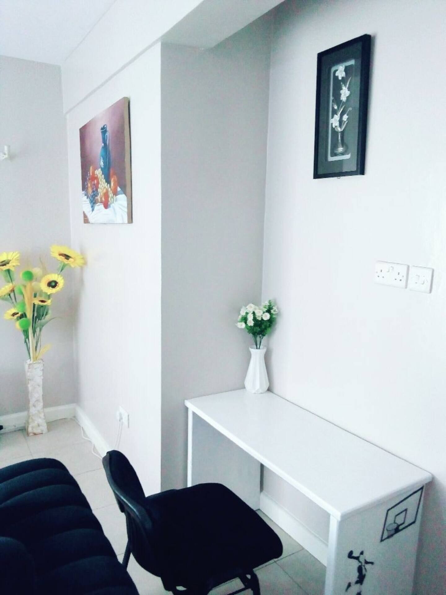 Una habitación moderna con un escritorio blanco, una silla de oficina negra y dos jarrones con flores.