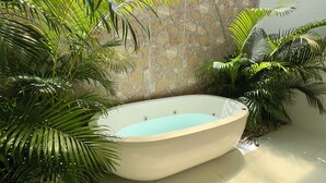 A spa area with a freestanding bathtub, surrounded by lush green plants and a stone wall. - Casa com Piscina Privativa e Hidromassagem #2 (Tibau do Sul)