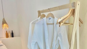 A white bathrobe hanging on a wooden rack in a room with a white wall, a wooden floor, and a hanging light fixture. - Casa com Piscina Privativa e Hidromassagem #2 (Tibau do Sul)