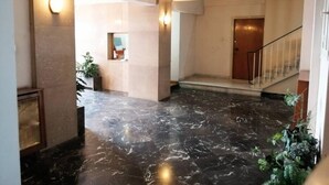 Um hall amplo com piso de mármore, uma escadaria e uma porta que dá acesso a outra área.