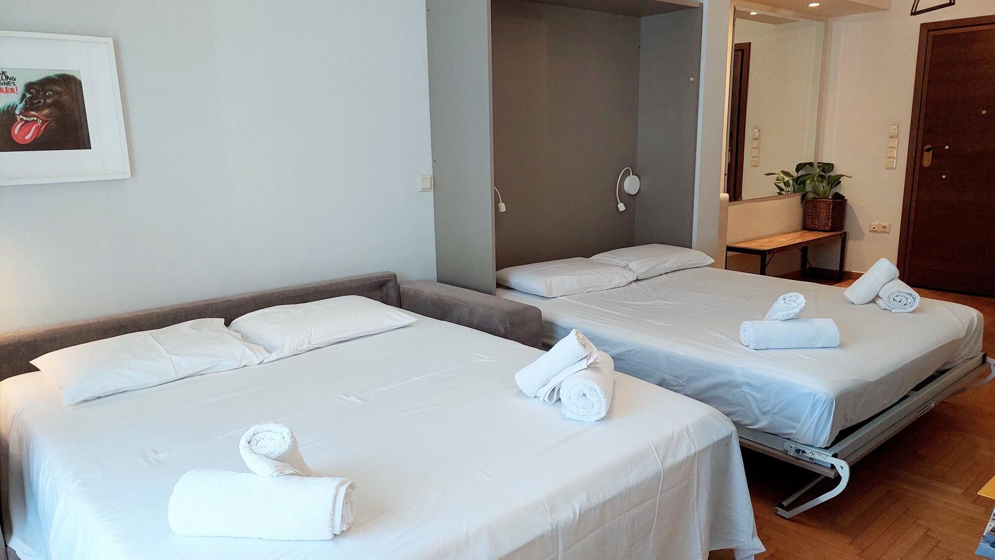 A hotel room with two beds, each with white linens and towels. There is a wooden headboard on the left bed, and a small table with a plant and a basket on the right.