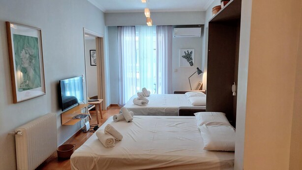 Quarto de hotel com duas camas, televisão, secretária e janela com cortinas.