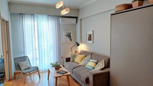 Uma sala de estar moderna com um sofá cinzento, uma poltrona cinza, uma mesa de centro de madeira e uma janela grande com cortinas leves.