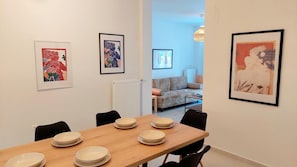 Uma área de refeições com uma mesa de madeira posta para quatro pessoas, quatro pratos brancos e cadeiras pretas. Há três obras de arte emolduradas nas paredes.