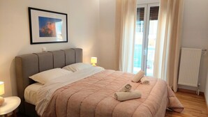 A neatly made bed with a pink quilt, two bedside lamps, and a framed picture on the wall. - Wonderful apartment in Acropolis (Athina)