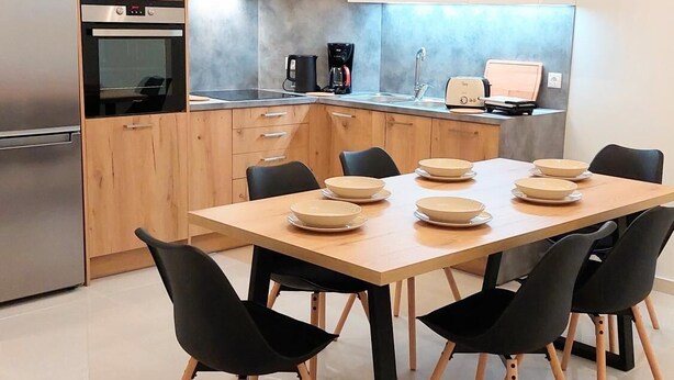 A modern kitchen with wooden cabinets, a built-in oven, a coffee maker, and a dining table with chairs. - Wonderful apartment in Acropolis (Athina)