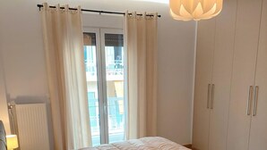 A bedroom with a bed, a bedside table with a lamp, a wardrobe, and a window with curtains. - Wonderful apartment in Acropolis (Athina)