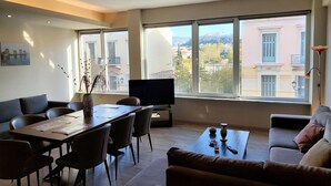 Una sala de estar moderna con comedor, ventanas amplias con vista a la ciudad y un televisor de pantalla plana.