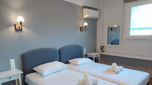 Habitación de hotel con dos camas, una mesita de noche, aire acondicionado, un espejo y una ventana.