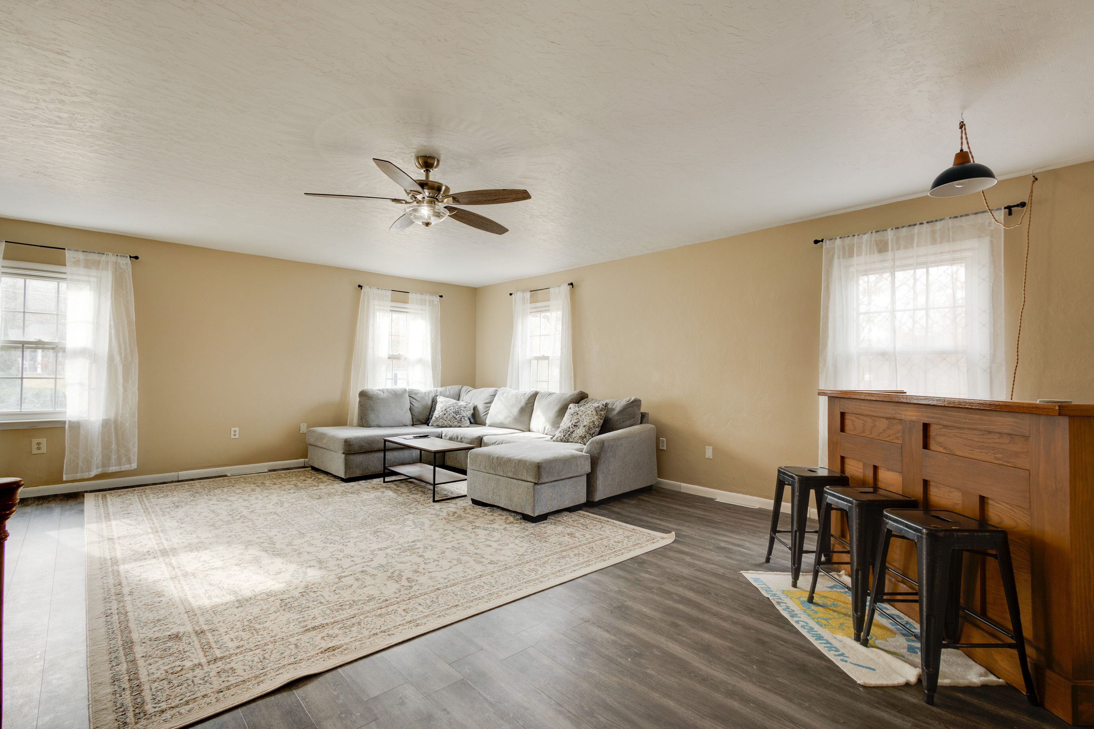 A spacious living room with a gray sectional sofa, a coffee table, and a wooden bar area with stools.
