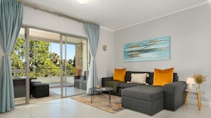 A modern living room with a grey sectional sofa, a coffee table, and a large window with curtains. - Comfort Living In The Heart Of Century City (Cape Town)