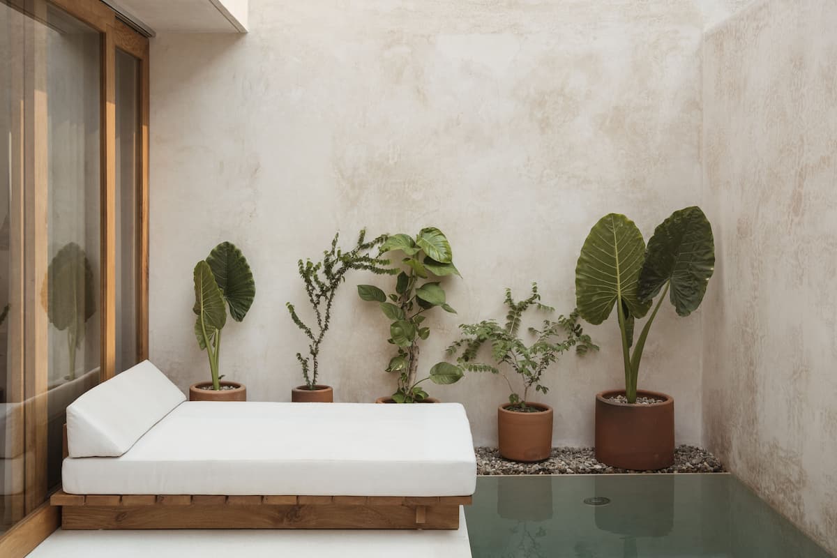 Un pequeño balcón privado con un banco acolchado blanco, diversas plantas en macetas y una mesa de vidrio.