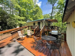 A wooden deck with outdoor furniture, a grill, and a staircase leading to a covered area.