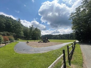 Un parque con un sendero pavimentado, juegos infantiles y una cerca de madera.
