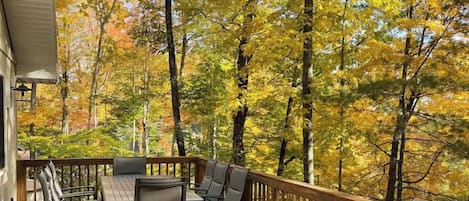 A wooden deck with a table and chairs, surrounded by trees with autumn foliage.