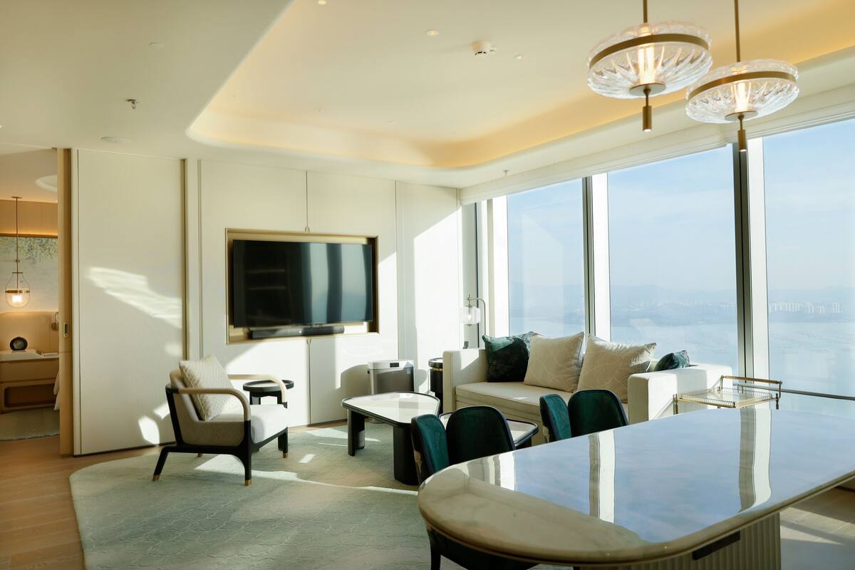 A modern living room with a large flat-screen TV, comfortable seating, and a large window offering a view of the city.