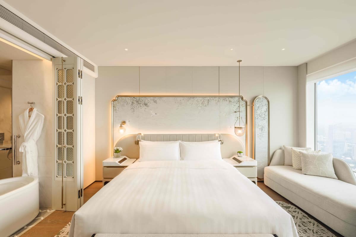 A modern hotel room with a large bed, a sitting area, and a view of the city.