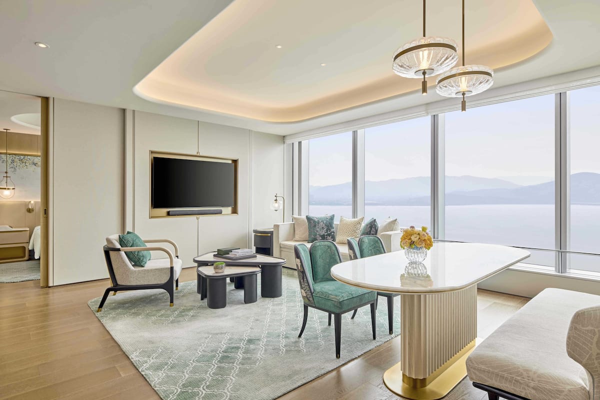 A modern living room with a large window, a flat-screen TV, and a dining area with a white table and chairs.