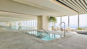 A modern indoor pool area with a clear view of the mountains in the background, a seating area with chairs and a table, and a large potted plant. - Shangri-La Nanshan, Shenzhen (Shenzhen)